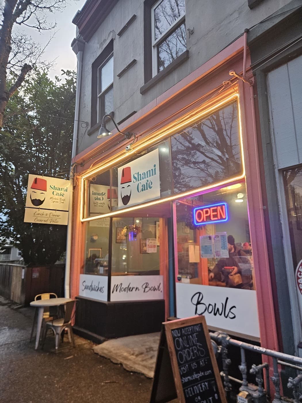 An illuminated cafe storefront sign at dusk with the letters and the awning lighting lit