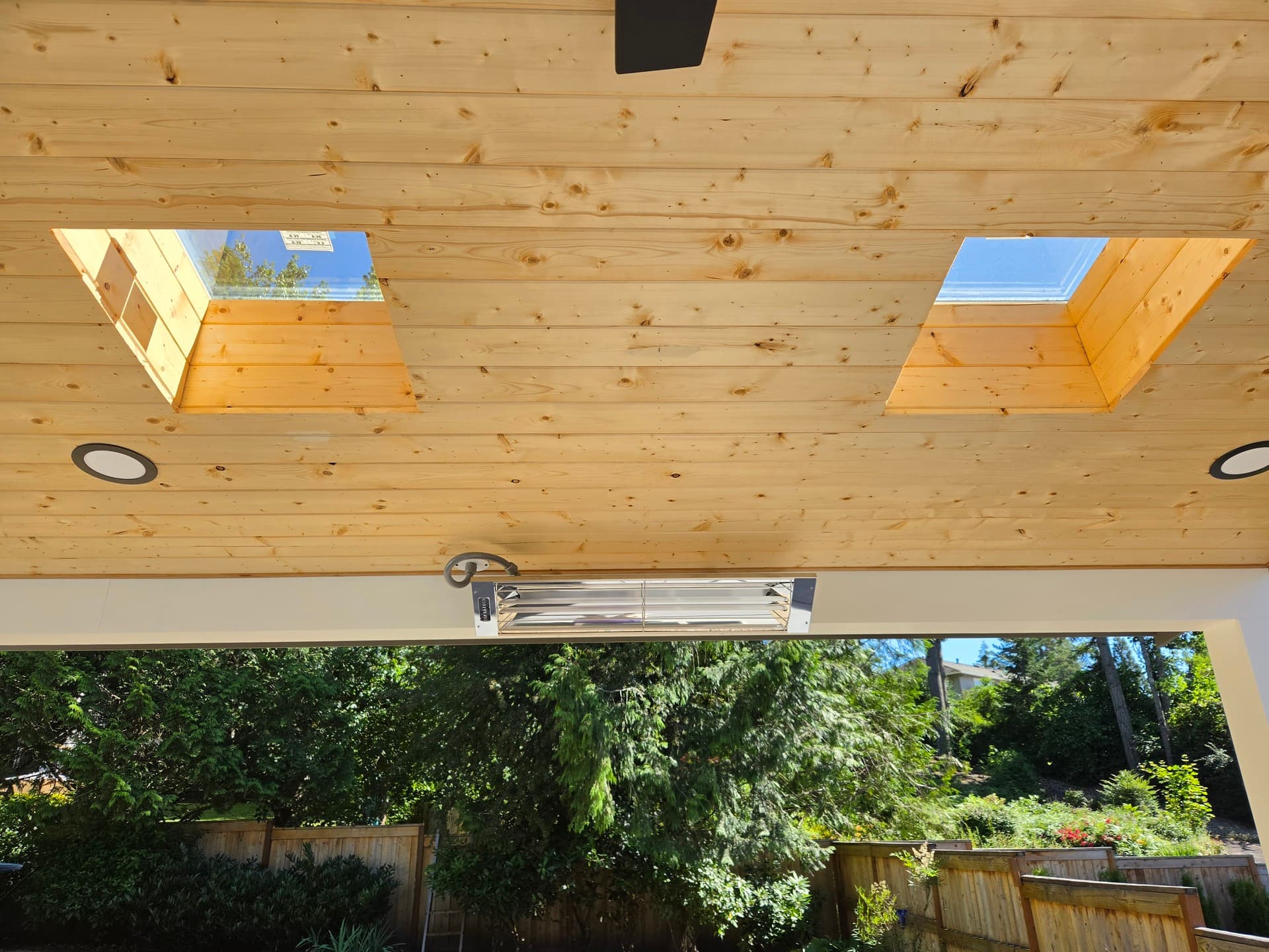 Two skylights set into the cedar ceiling of a covered patio, with recessed cans and a heater alongside