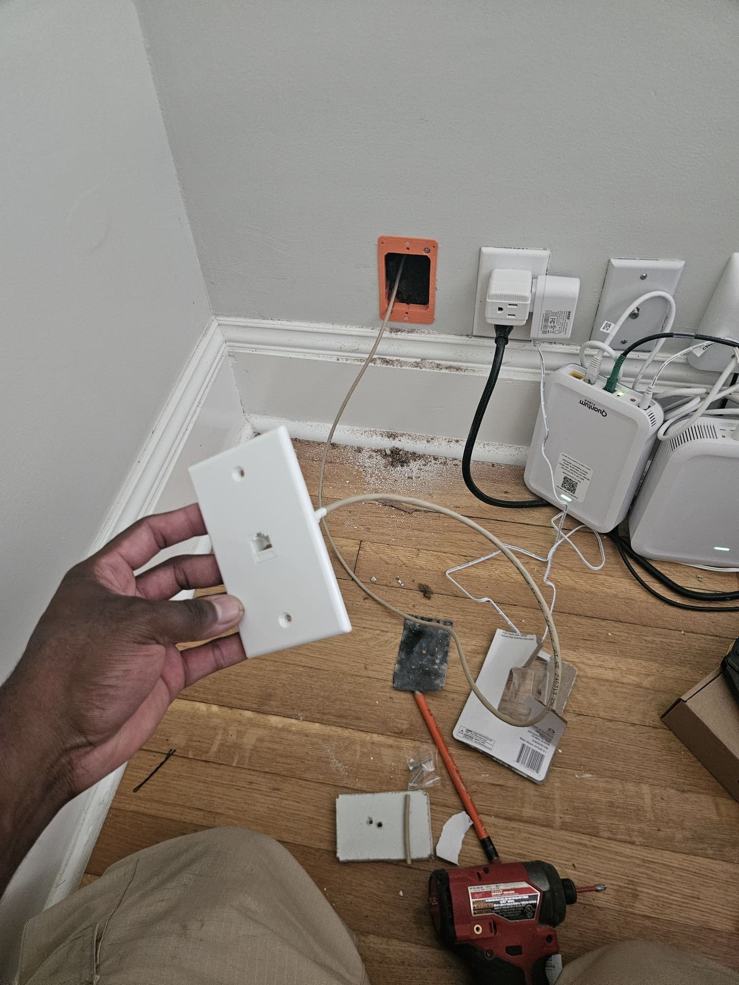 An electrician holding a wall plate while replacing a failed device, the burnt original set aside on the floor