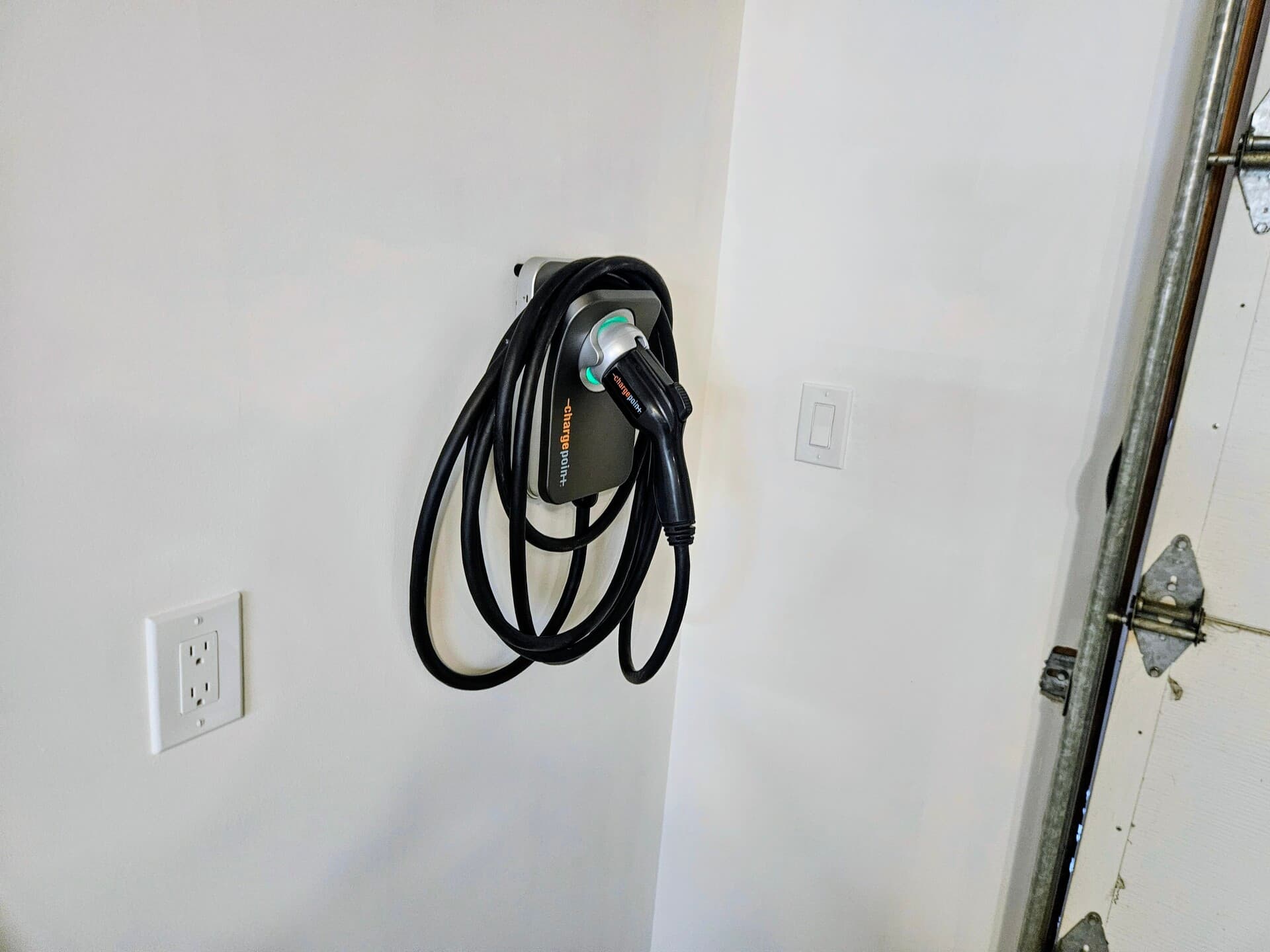 A Level 2 EV charger mounted on a garage wall with its cable coiled and the outlet set beside it