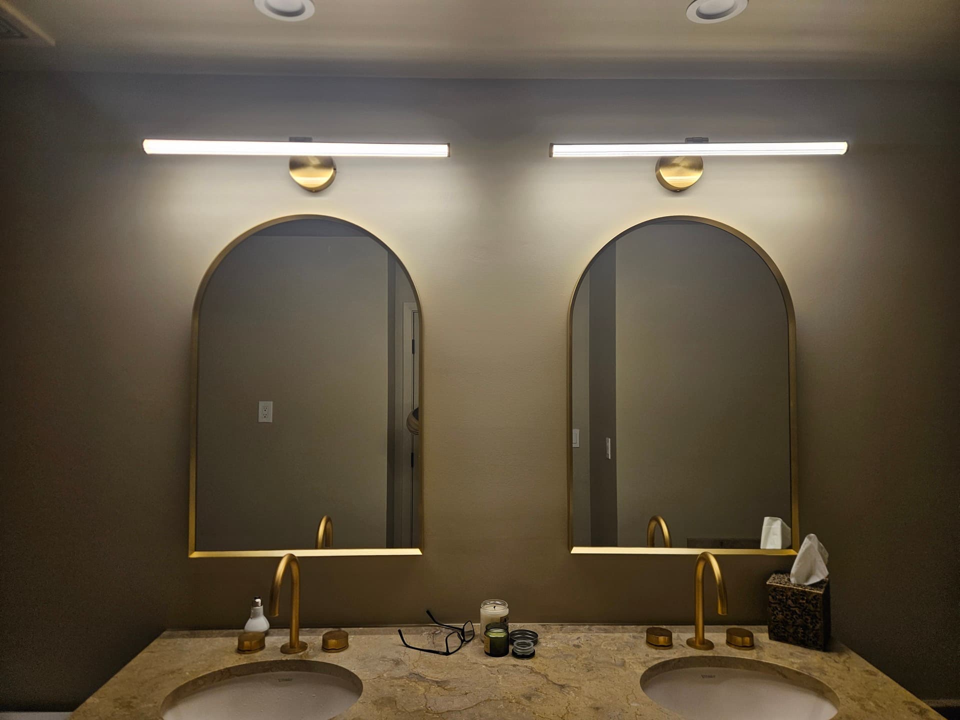 Two arched brass mirrors under linear LED vanity bars in a finished bathroom remodel