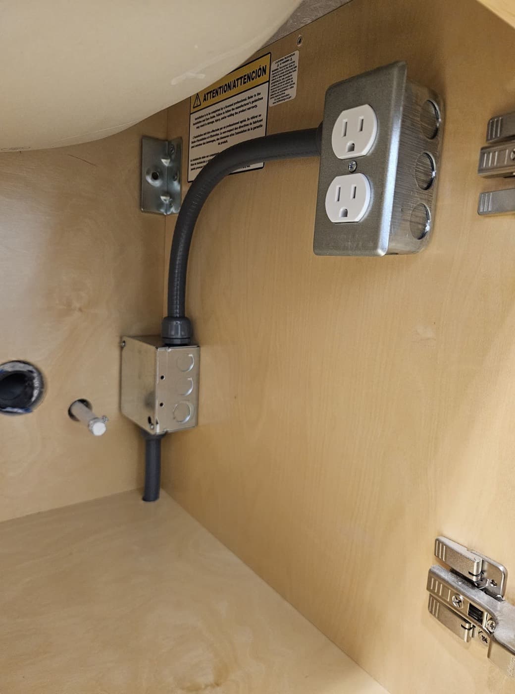 A duplex receptacle and junction box mounted inside a cabinet under a kitchen sink