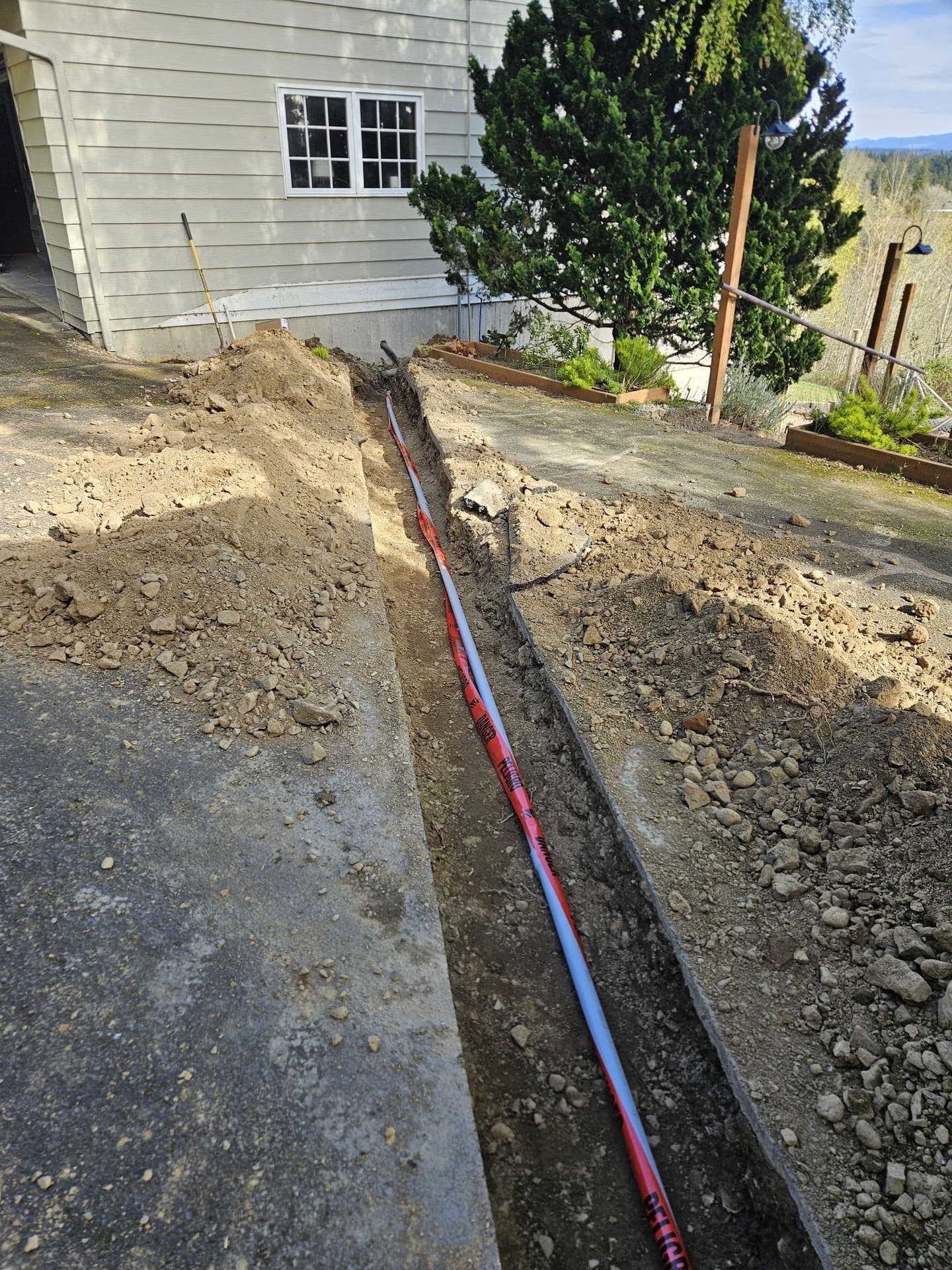 A trench cut across a driveway with the underground conduit laid in and warning tape run above it