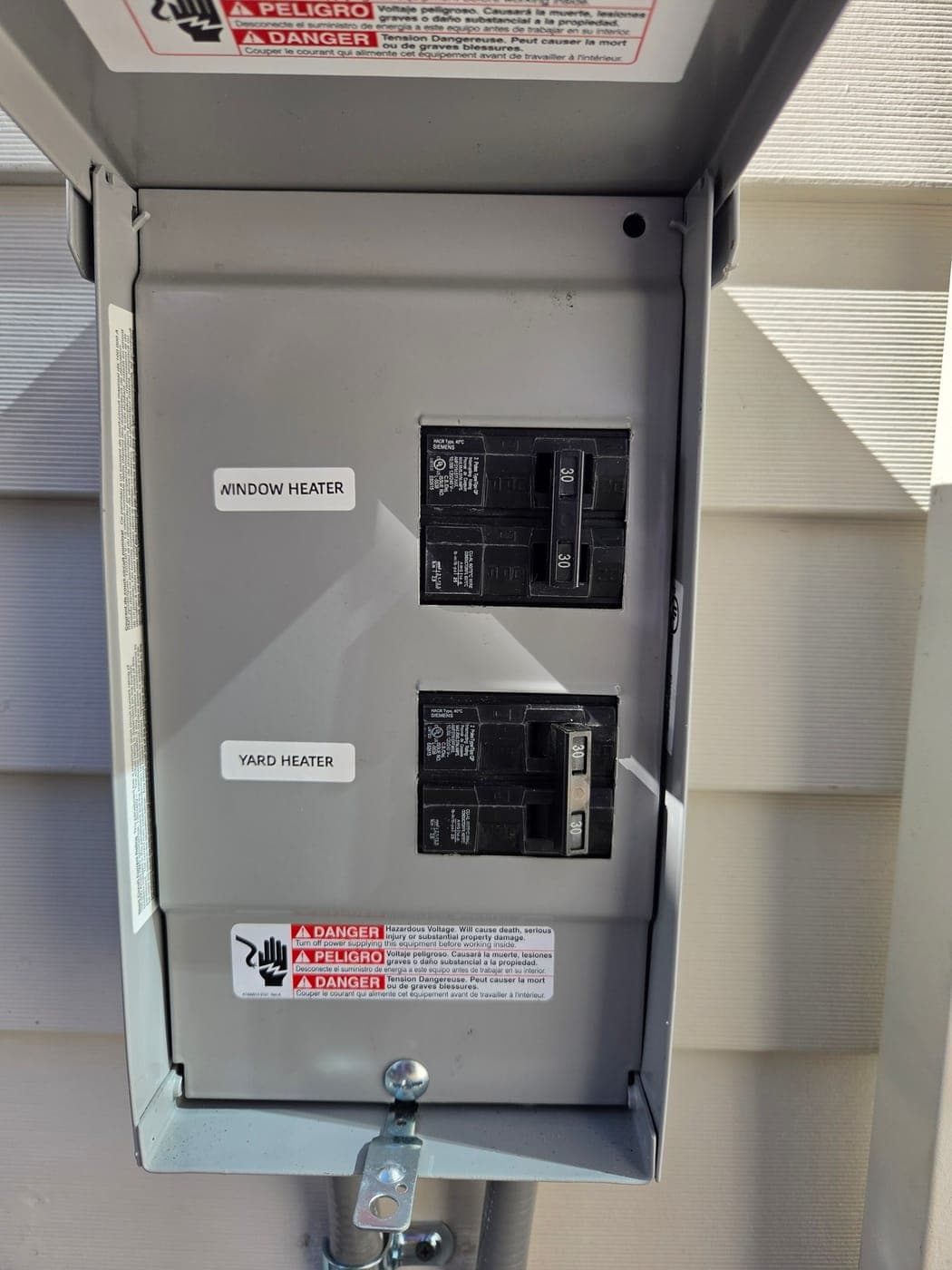 An exterior subpanel with its two breakers labelled by hand, window heater and yard heater