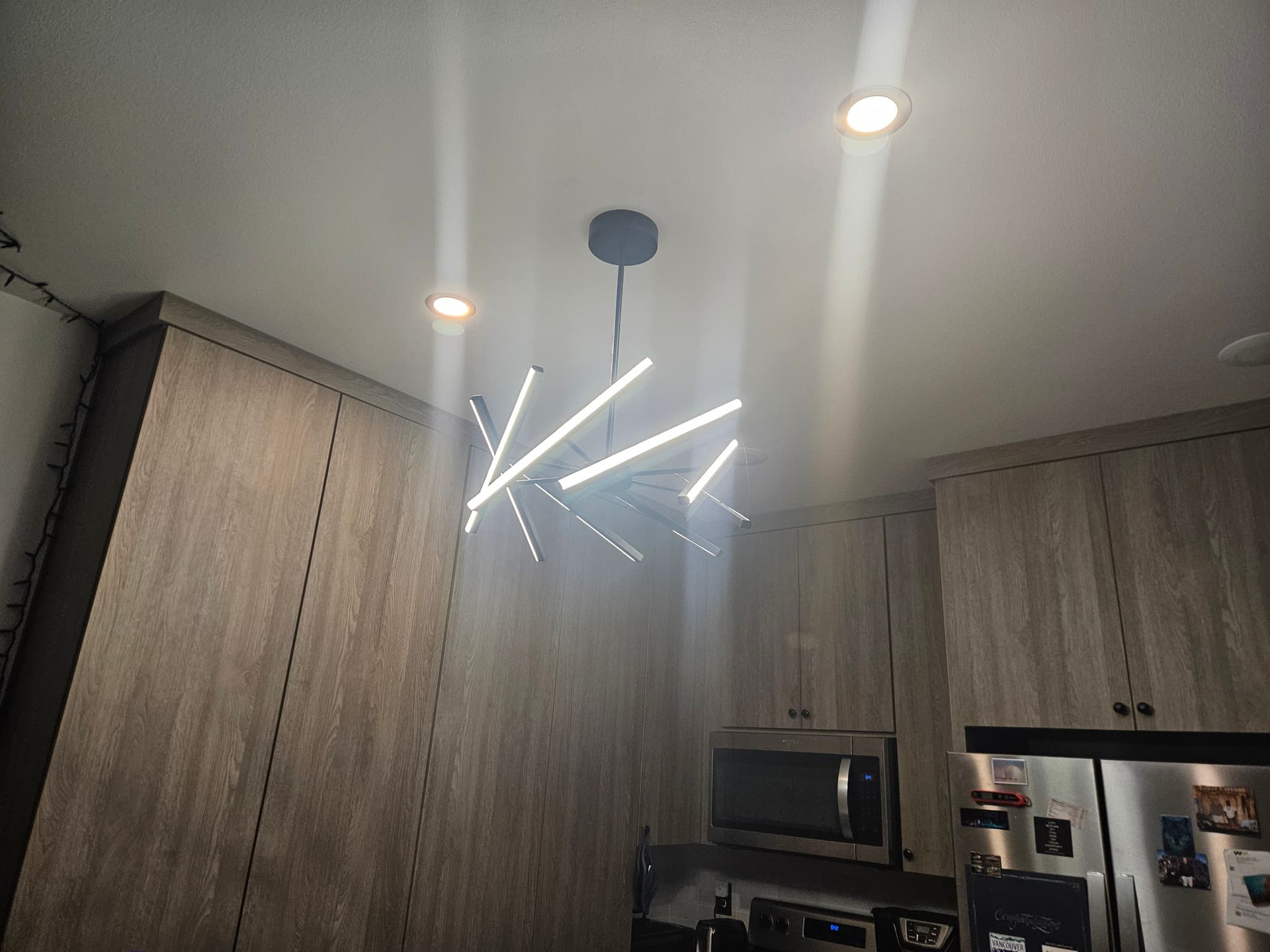 A multi-arm linear LED pendant lit over a kitchen beside warm under cabinet strips