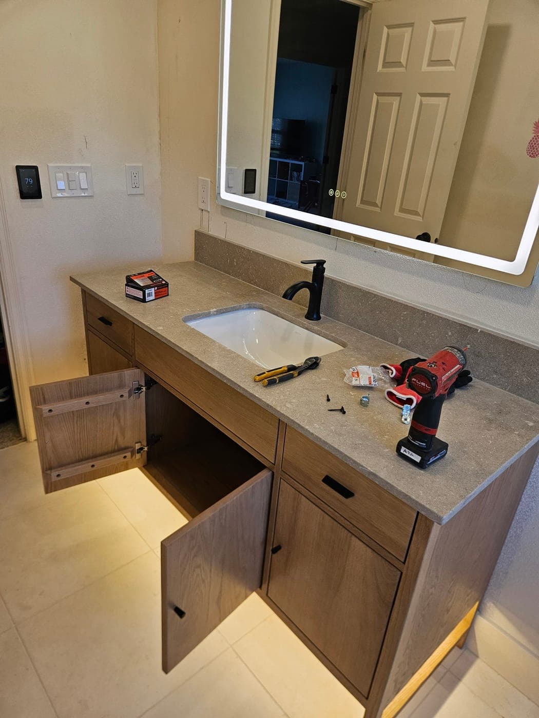 A bank of new switches and dimmers on a bathroom wall beside a lit mirror